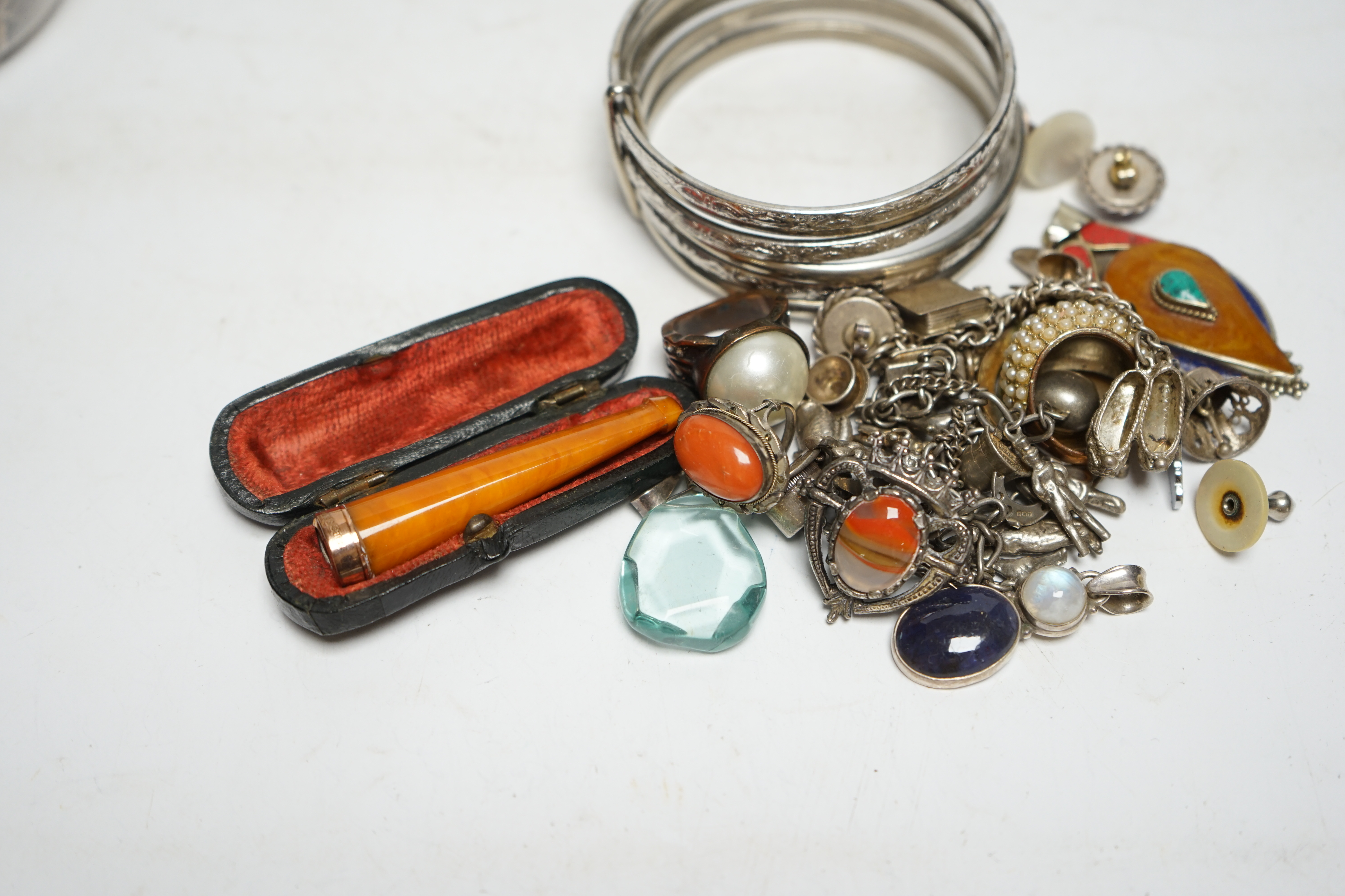 A small group of assorted white metal and costume jewellery including two charm bracelets and a cased 9ct gold mounted amber cigarette holder. Condition - poor to fair